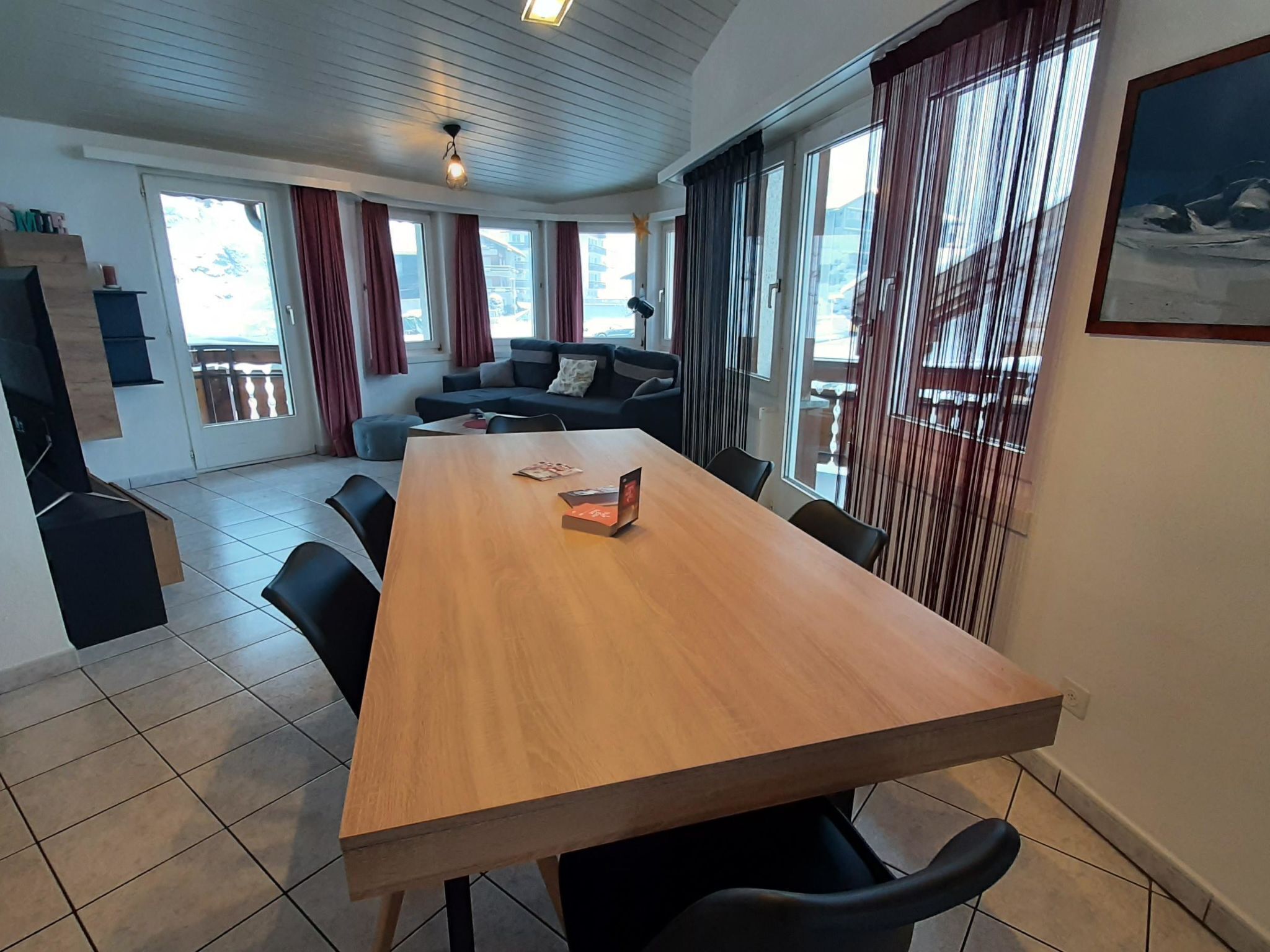 Een ruime kamer met een grote houten tafel, zwarte stoelen, een bank en een balkon met uitzicht.