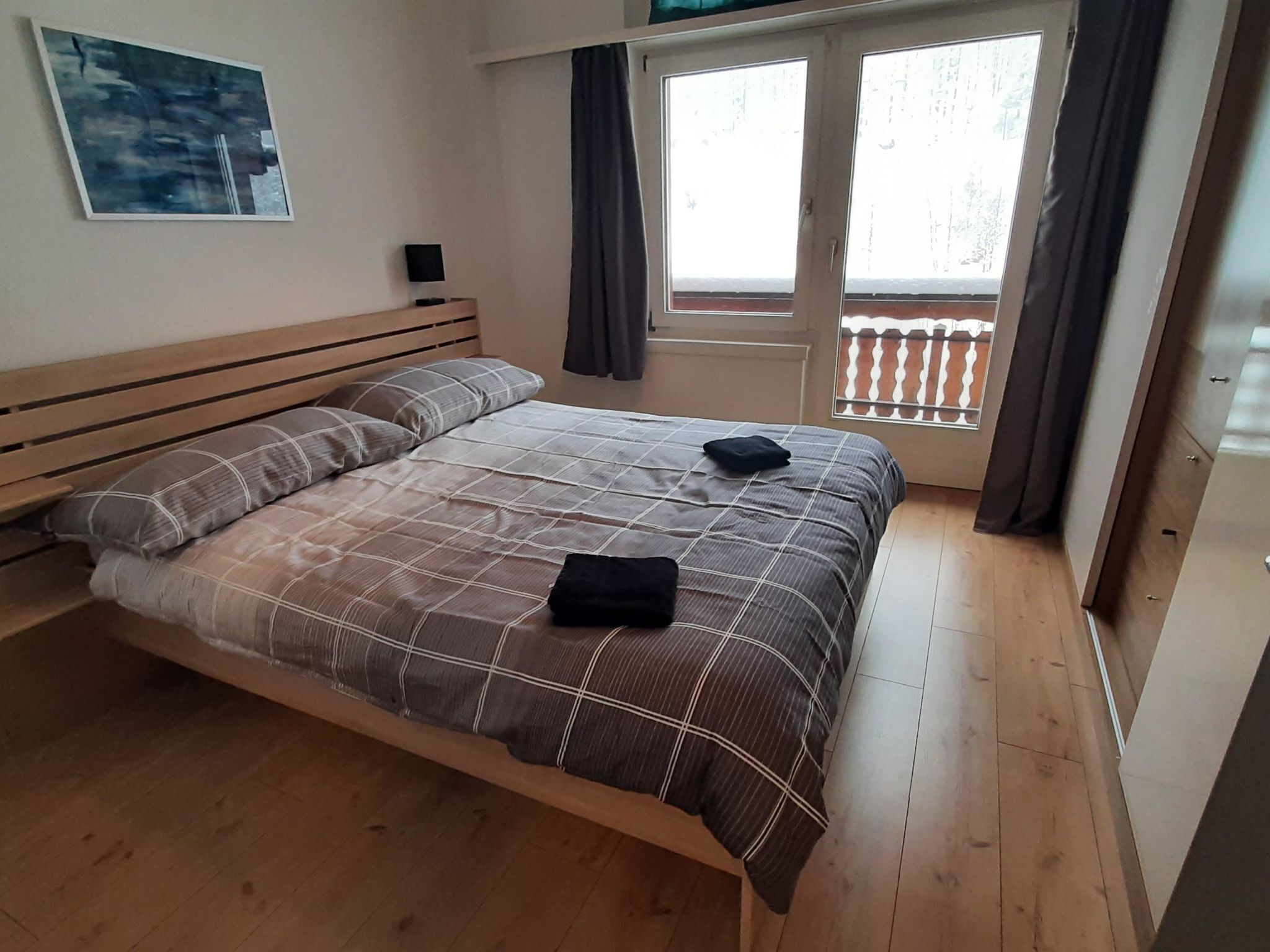 A bedroom with a wooden bed, a nightstand, a window with curtains, and a view of the outside.