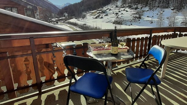 En balkon med et bord dækket til to, med udsigt over et sneklædt bjerglandskab.