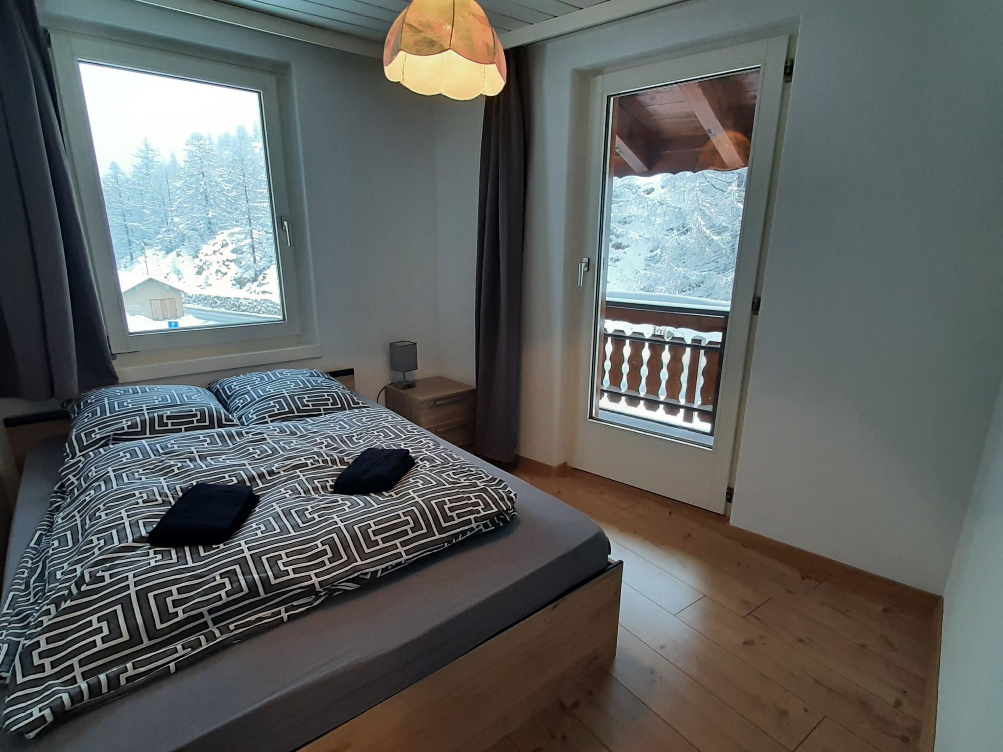 A bedroom with a bed, two pillows, a nightstand, a lamp, and a window with a view of snow-covered trees.