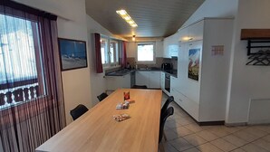 En spiseplads med et langt træbord, stole og udsigt ud af et vindue med gardiner.