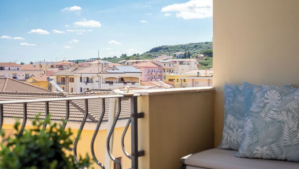 Ein Balkon mit Blick auf eine Wohngegend, ein Sofa mit einem gemusterten Kissen und ein Geländer.