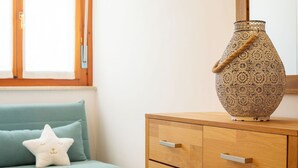 Ein Zimmer mit einem türkisfarbenen Sofa, einem weißen sternförmigen Kissen, einem Holzkabinett mit Schubladen und einer dekorativen Vase.