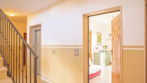 Ein Flur mit einer Treppe, einer zur Kammer mit einem Bett führenden Tür und einem Schrank mit darin befindlichen Gegenständen.