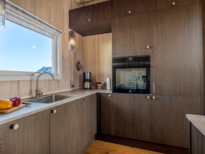 Una cocina moderna con armarios de madera, horno empotrado, cafetera y ventana que aporta luz natural.
