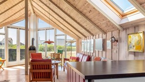 A spacious room with a high ceiling, wooden beams, a large window, a sofa, a dining table, and a kitchen area. - "Eldmar" - 500m from the sea by Interhome (Harboøre)