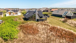 A coastal residential area with modern houses, some with sloped roofs and large windows, surrounded by grassy dunes and a clear sky. - "Eldmar" - 500m from the sea by Interhome (Harboøre)