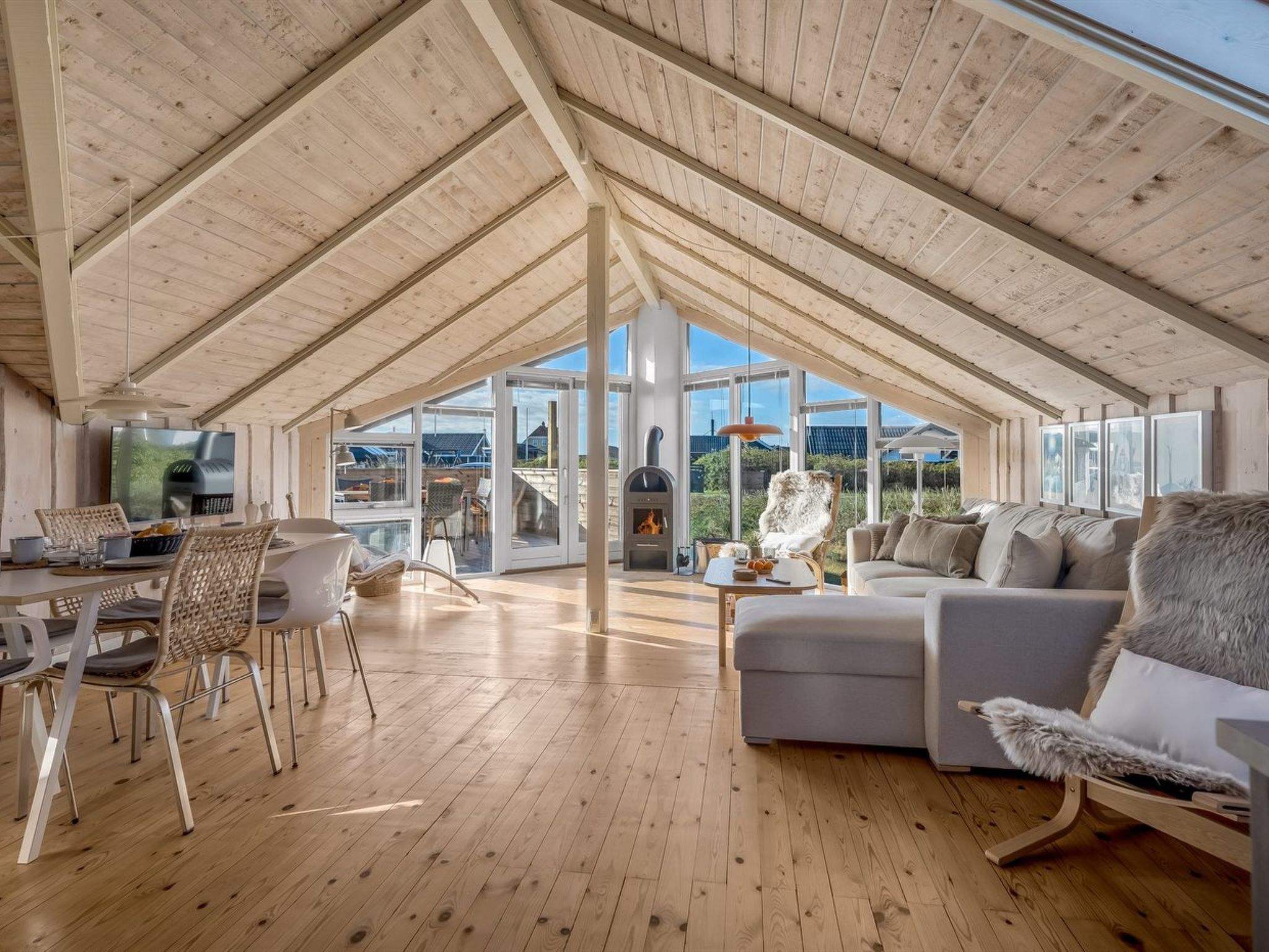 A spacious loft with a high ceiling, wooden beams, a dining area, a sofa, and a fireplace.