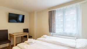Een hotelkamer met een bed, een bureau, een stoel, een televisie en een raam met gordijnen.