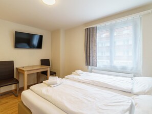 Ein Hotelzimmer mit Bett, Schreibtisch, Stuhl, Fernseher und einem fenster mit Vorhängen.