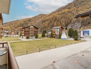 Ein Hotel mit mehreren Etagen, einem Parkplatz und Blick auf eine Berglandschaft mit herbstlich gefärbten Bäumen.