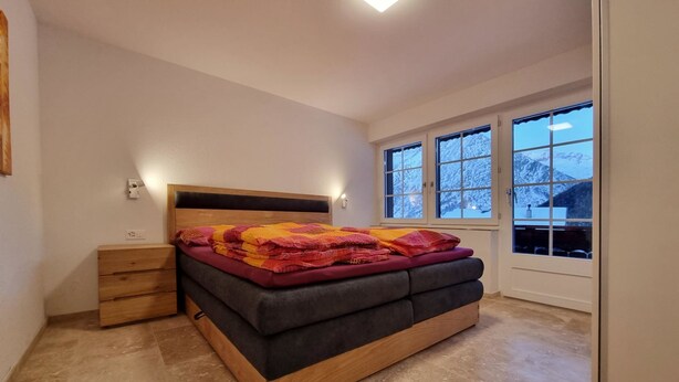 Ein Schlafzimmer mit Bett, Nachttischen, einem Fenster und Blick auf schneebedeckte Berge.