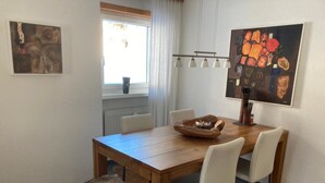 A dining area with a wooden table, white chairs, a fur-covered ottoman, and artwork on the walls. - Vallesia Appartement/Fewo Appartement/Fewo by Interhome (Saas-Fee)