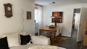 A living room with a sofa, a dining table with chairs, a clock on the wall, and a painting above the table. - Vallesia Appartement/Fewo Appartement/Fewo by Interhome (Saas-Fee)