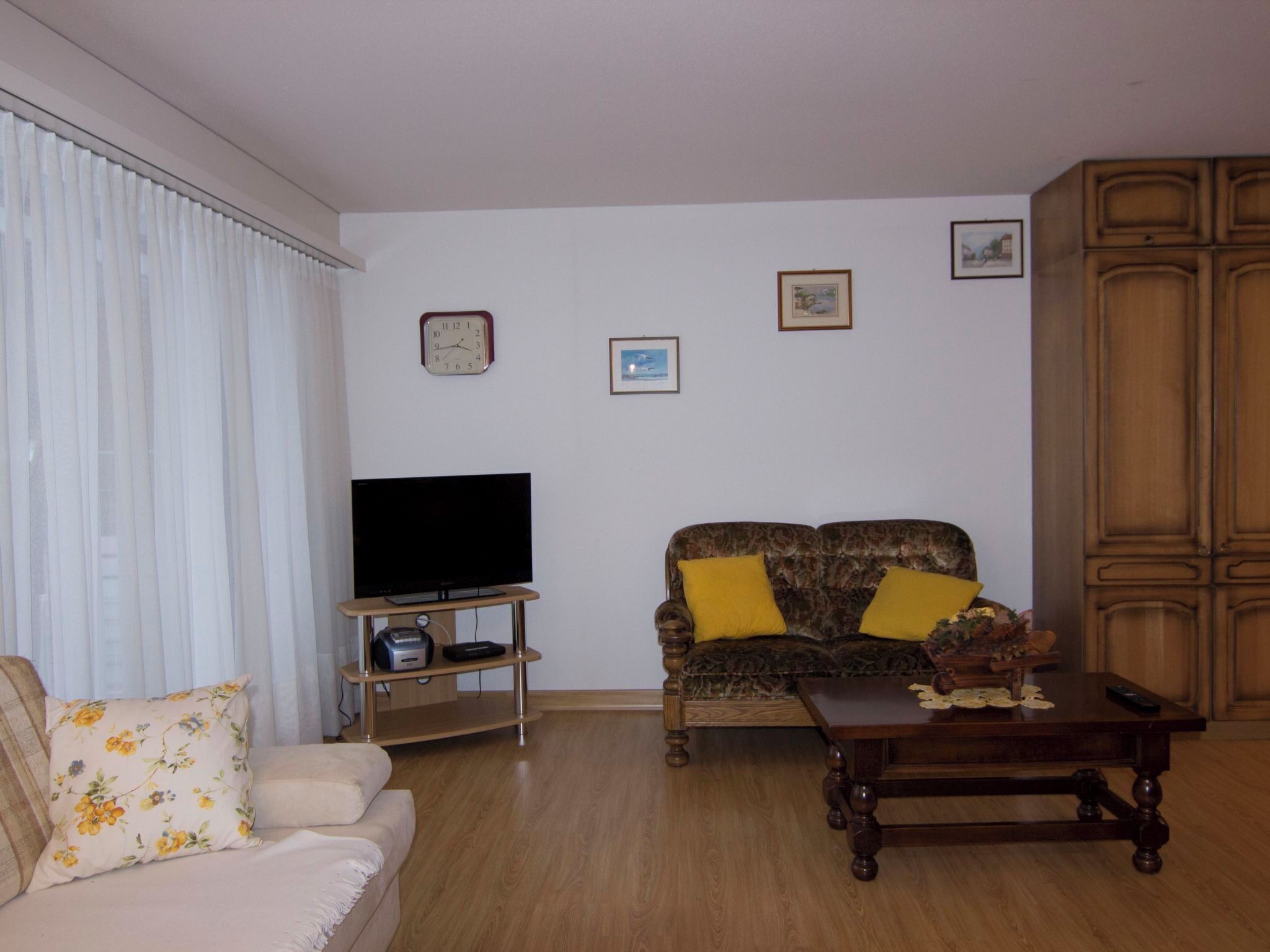 Uma sala de estar com um sofá, uma televisão sobre um móvel, uma mesa de centro e um armário.