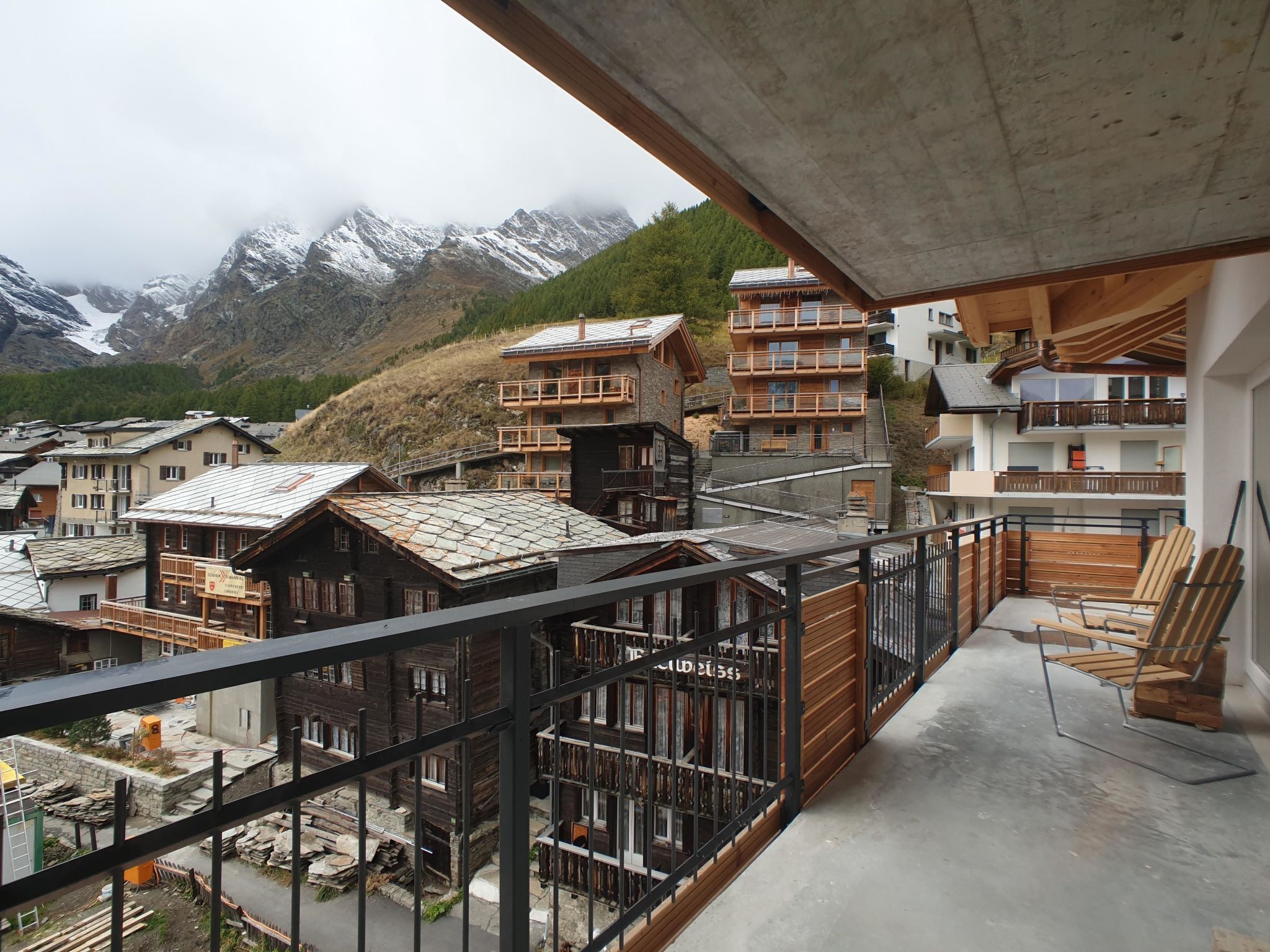 Un balcon offrant une vue sur des bâtiments traditionnels en bois et sur un paysage montagneux en arrière-plan.