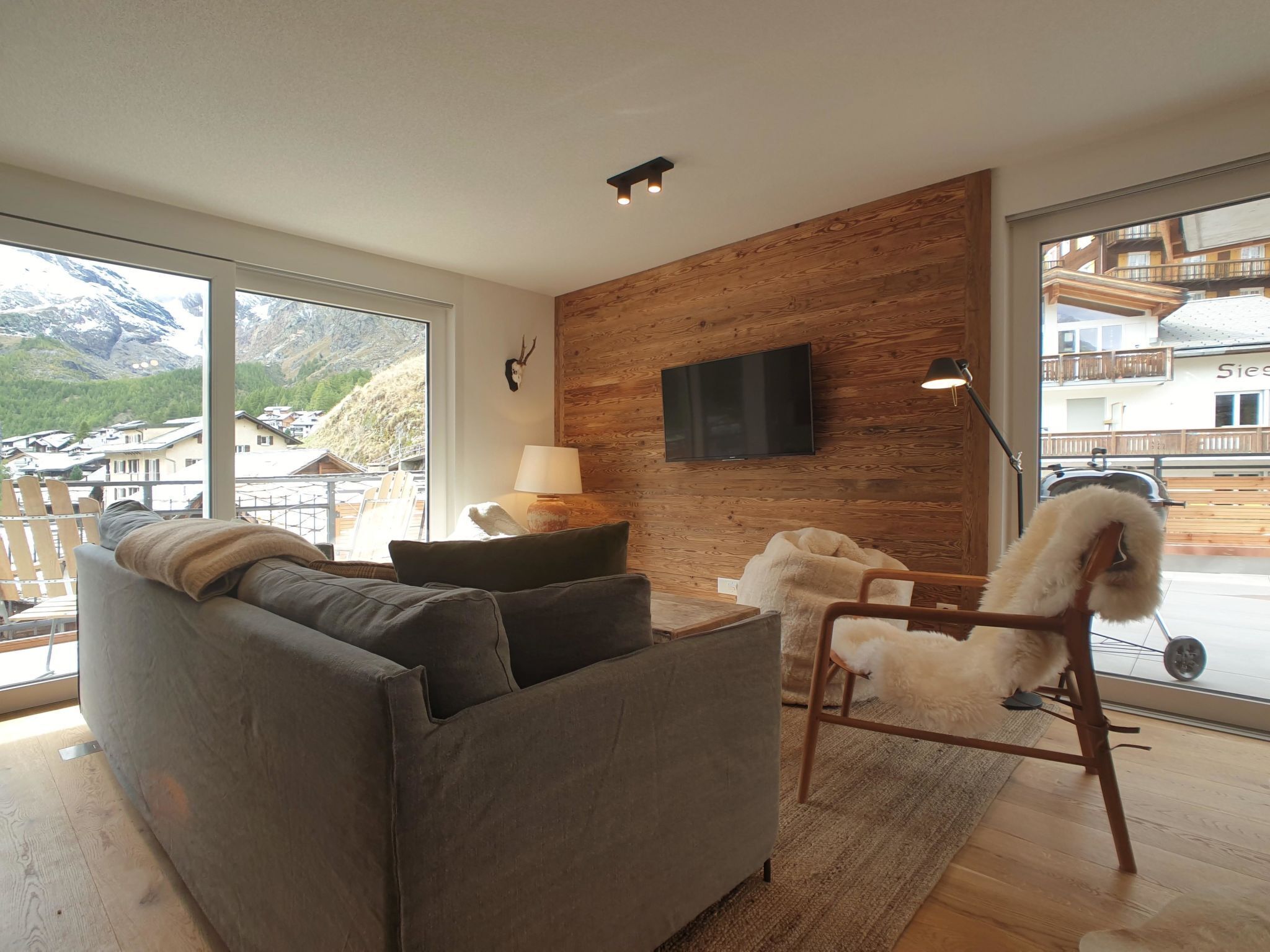 Een moderne woonkamer met een grijze bank, een witte vacrastad, een tv aan de wand, en een houten wand.