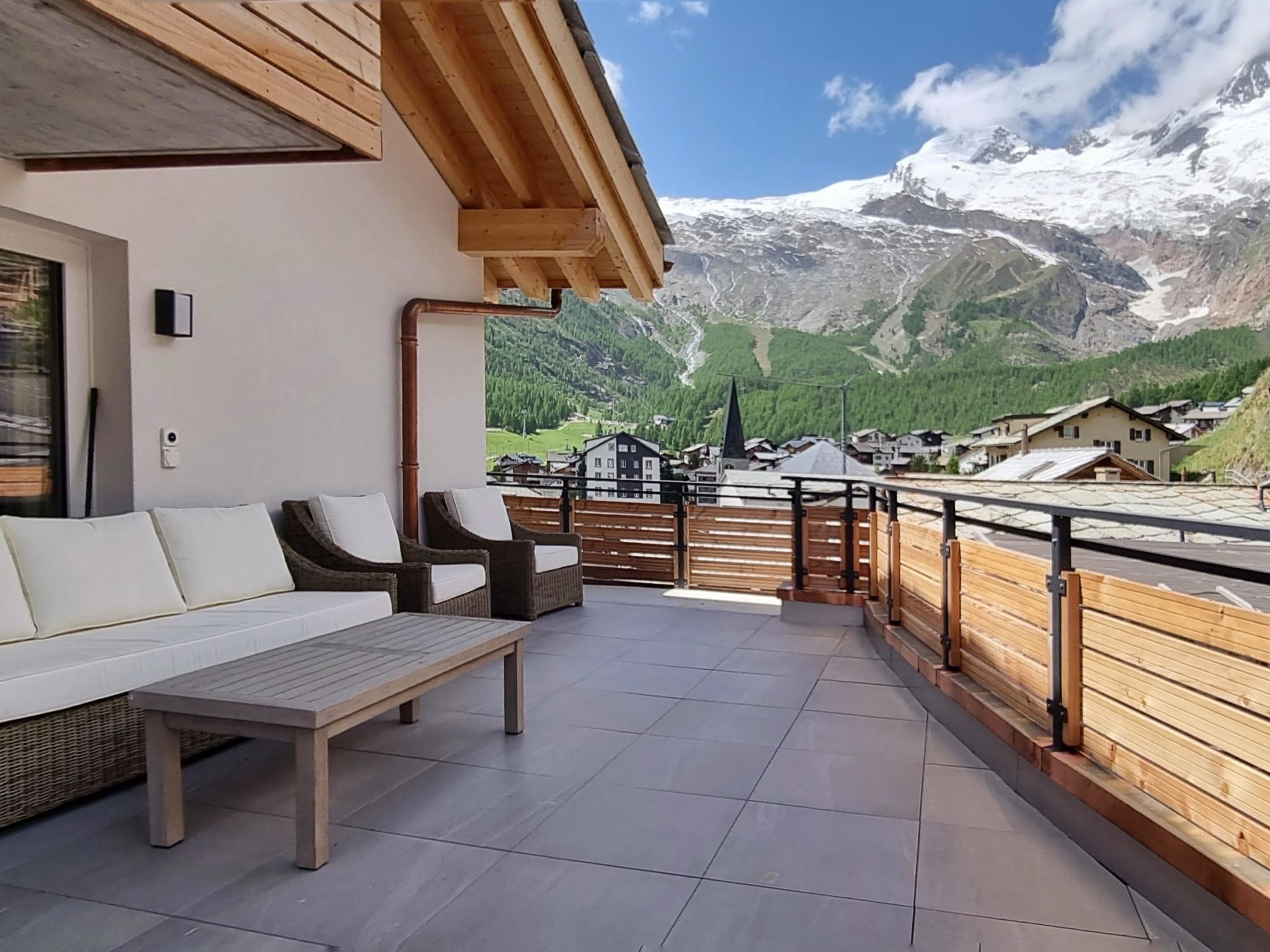 Un balcone con vista su una catena montuosa, una recinzione in legno e mobili da esterno.