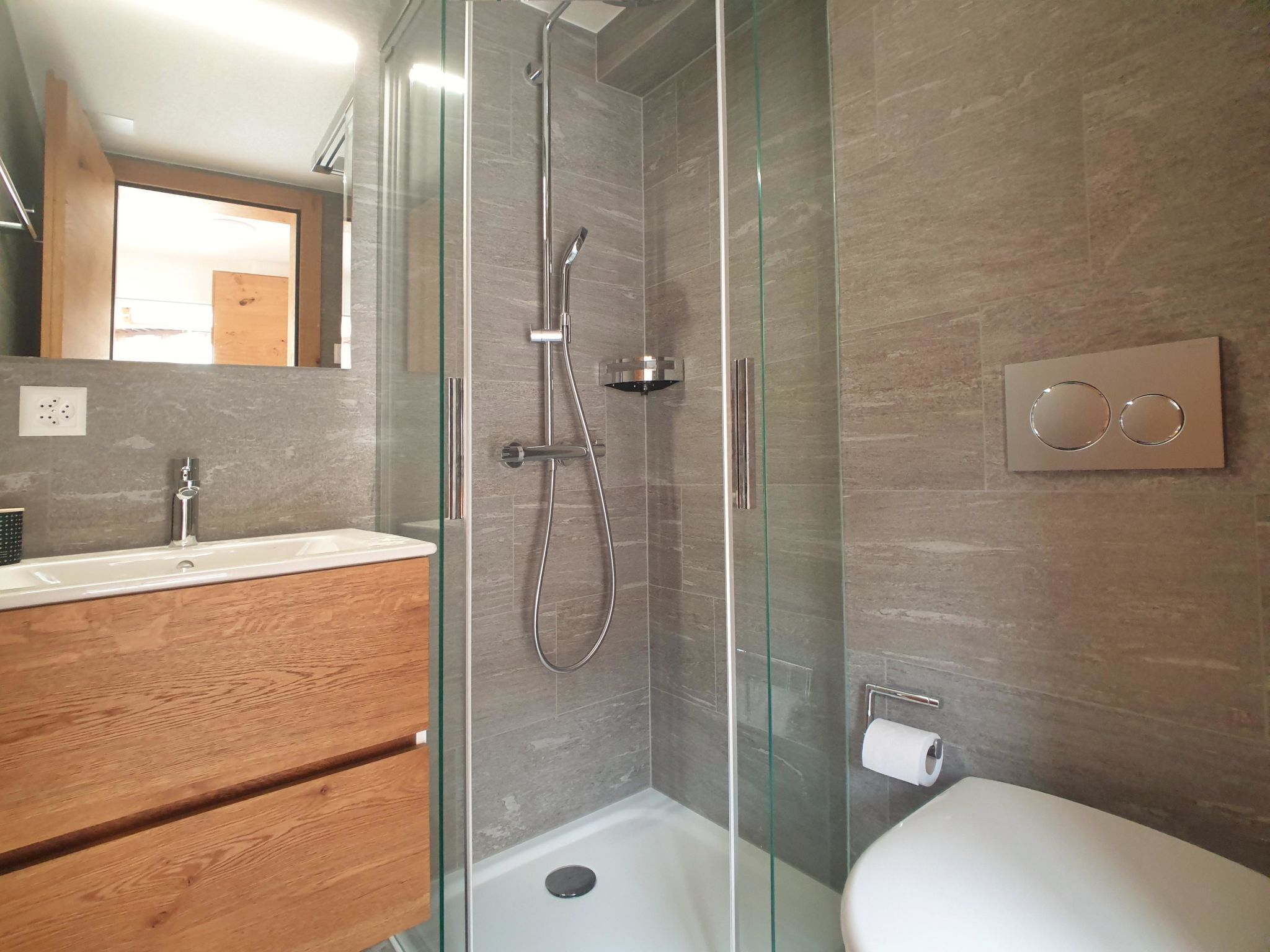 Een moderne badkamer met een douchecabine van glas, een houten wastafelmeubel en een toilet.