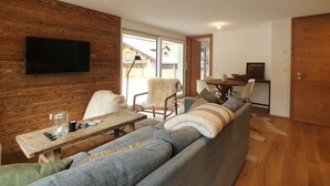 Una sala de estar moderna con una pared de madera, un sofá gris grande, una mesa de centro de madera y un televisor de pantalla plana montado en la pared.