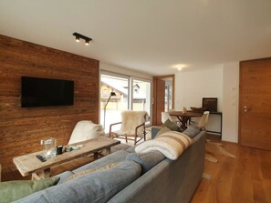 A modern living room with a wooden wall, a large grey sofa, a wooden coffee table, and a flat-screen TV mounted on the wall. - Britannia Appartement/Fewo 4-Bettwohnung by Interhome (Saas-Fee)