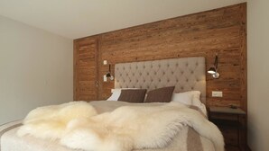 Un dormitorio con cabecera capitonada, una colcha blanca mullida y pared de paneles de madera.