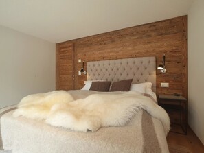 A bedroom with a tufted headboard, a fluffy white blanket, and a wooden panel wall. - Britannia Appartement/Fewo 4-Bettwohnung by Interhome (Saas-Fee)