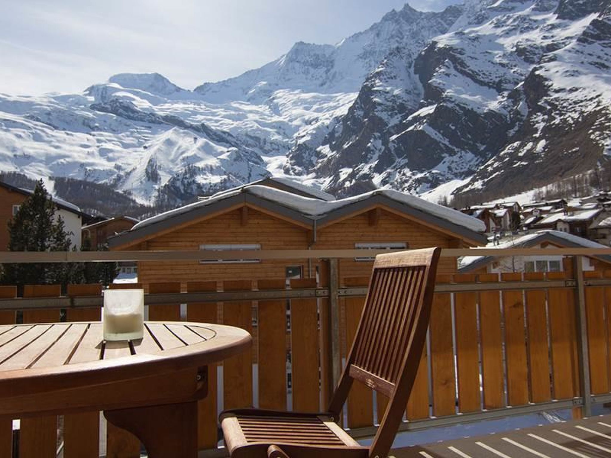A wooden deck with a table and a chair, overlooking a snow-covered mountain range.