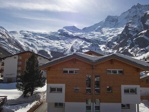 A wooden chalet with a mountain backdrop, featuring a clear sky and snow-covered peaks. - Perla Appartement/Fewo 6-Bettwohnung Nr. 1 by Interhome (Saas-Fee)