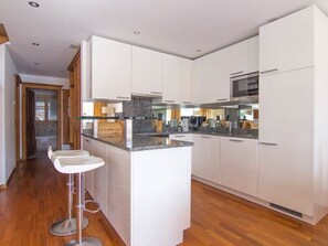 Eine moderne Küche mit weißen Schränken, einer zentralen Kochinsel mit Barhocker und einer Edelstahl-Dunstabzugshaube.