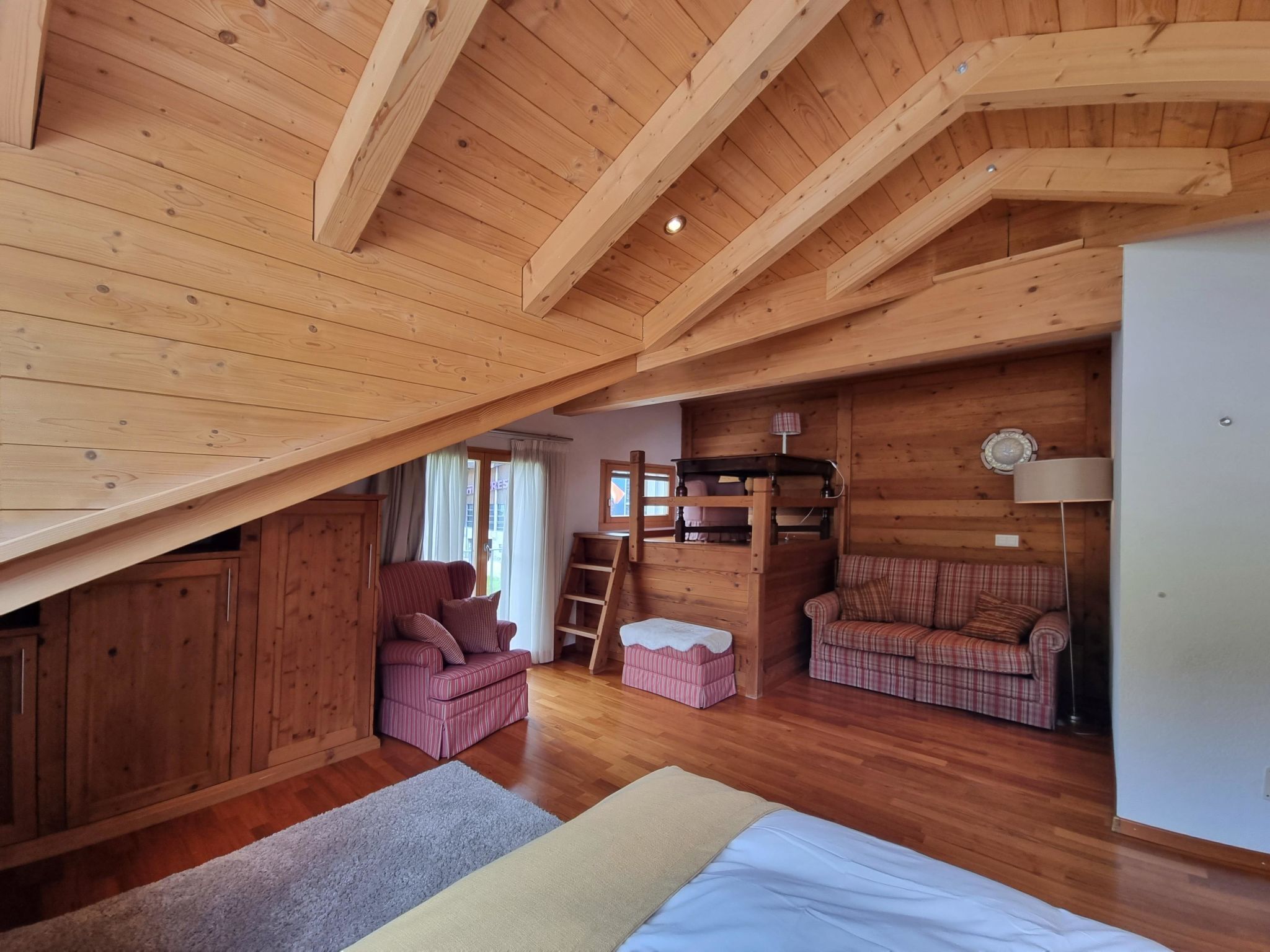 Un interior de madera con una litera, dos sofás escoceses, una silla y un armario.