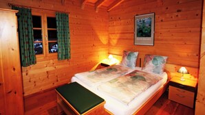 A wooden cabin bedroom with a bed, two bedside tables, a bench, and a window with curtains. - Les Mélèzes Appartement/Fewo 8-Bettwohnung by Interhome (Saas-Fee)