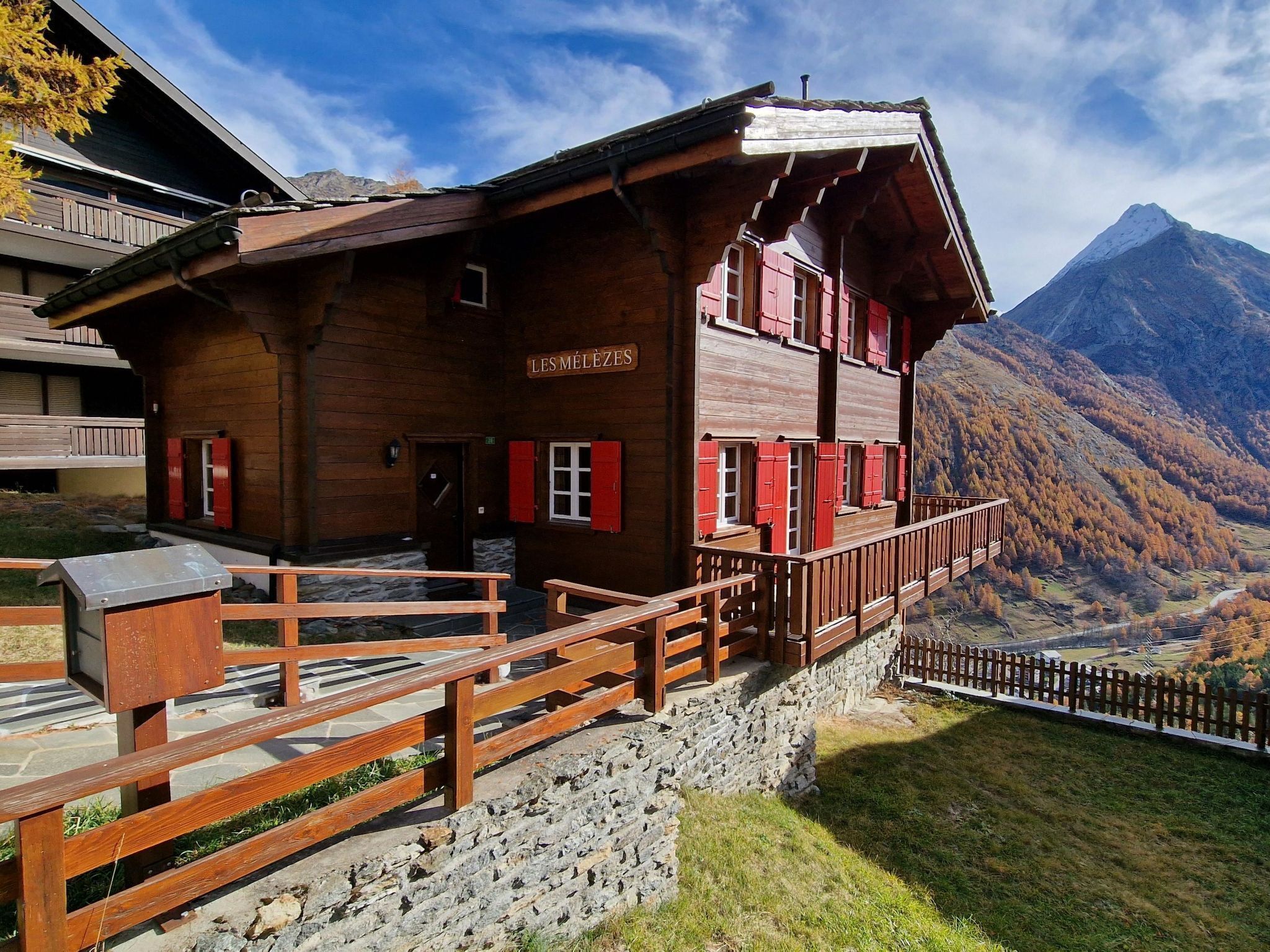 Un chalet en bois doté d’un balcon, d’un mur en pierre et offrant une vue sur la montagne.
