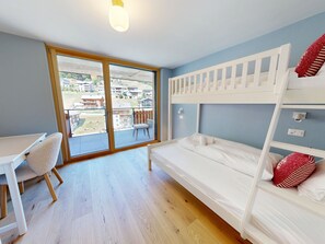 Ein Zimmer mit einem Etagenbett, einem Schreibtisch und einem Stuhl. Ein großes Fenster bietet Blick auf Gebäude.