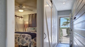 A hallway leading to a bedroom with a bed, a ceiling fan, and a view of the outside. - Waterfront Hideaway | Patio, Pool & Fishing Dock (Corpus Christi)