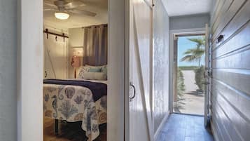 A hallway leading to a bedroom with a bed, a ceiling fan, and a view of the outside.