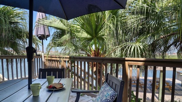 A wooden deck with a table and chairs, a bench, and a view of the water. - Waterfront Hideaway | Patio, Pool & Fishing Dock (Corpus Christi)
