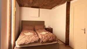 A bedroom with a wooden ceiling, a bed with a beige blanket, a bedside table, and a white door. - Sonnenhang 2 Appartement/Fewo Apartment Nr. 2 by Interhome (Saas-Fee)