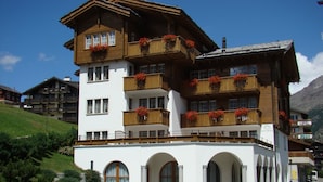 Ein mehrstöckiges Hotel mit Balkonen, Rundbogenfenstern und einer Bergkulisse im Hintergrund.