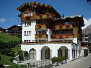 A multi-story hotel with balconies, arched windows, and a mountainous backdrop. - Arcade Appartement/Fewo 4-Bettwohnung Nr. 115C06 by Interhome (Saas-Fee)