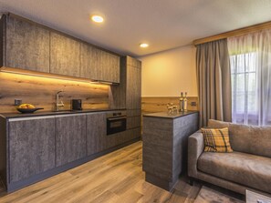 A modern kitchen with wooden cabinets, a built-in oven, and a dining area with a sofa and curtains. - Arcade Appartement/Fewo 4-Bettwohnung Nr. 115C06 by Interhome (Saas-Fee)