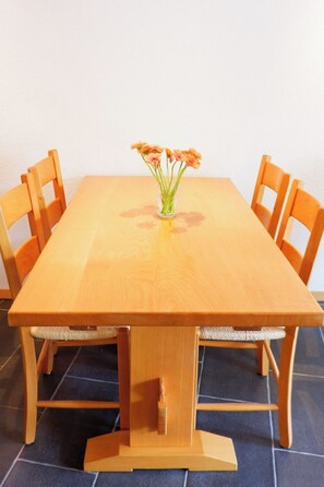 A wooden dining table with a vase of flowers in the center, surrounded by four chairs. - Haus Judith - Bonita Appartement/Fewo 2-Zimmerwohnung by Interhome (Saas-Fee)