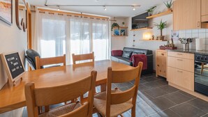Cozinha moderna com armários de madeira, uma mesa de jantar com cadeiras, um sofá e uma televisão montada acima do balcão.