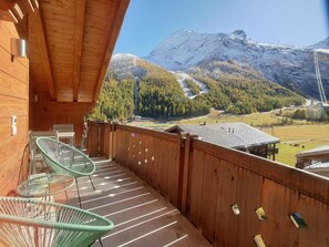 Ein Holzbalkon mit zwei grünen Stühlen und Blick auf einen Berg, bewölkter Himmel.