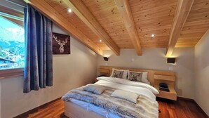 A bedroom with a wooden ceiling, a bed with a fluffy blanket, a window with curtains, and a wall-mounted light. - Aramis 5. OG Appartement/Fewo 6-Bettwohnung by Interhome (Saas-Fee)