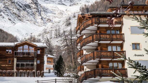 A hotel with wooden balconies, a mountain backdrop, and a sign reading 'Aramis.' - Aramis 5. OG Appartement/Fewo 6-Bettwohnung by Interhome (Saas-Fee)