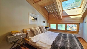 A bedroom with a bed, a bedside table, a lamp, a framed picture, and a window with a view. - Aramis 5. OG Appartement/Fewo 6-Bettwohnung by Interhome (Saas-Fee)
