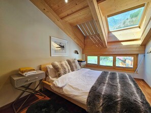 A bedroom with a bed, a bedside table, a lamp, a framed picture, and a window with a view. - Aramis 5. OG Appartement/Fewo 6-Bettwohnung by Interhome (Saas-Fee)