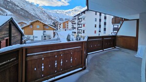 Vista desde un balcón con edificios nevados y montañas al fondo.