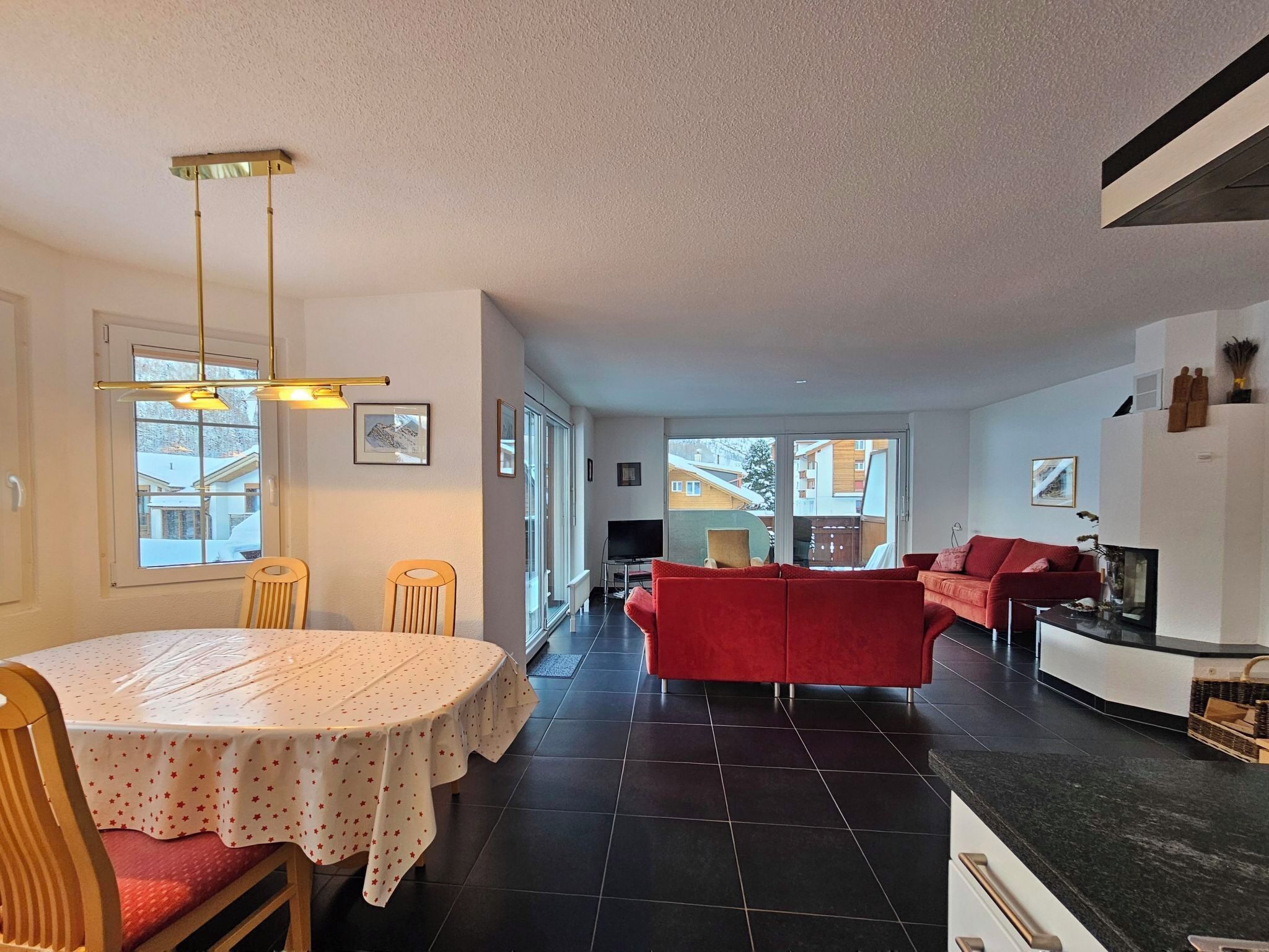Una sala de estar moderna con un sofá rojo, un comedor con mesa y sillas, y una cocina con encimera negra.